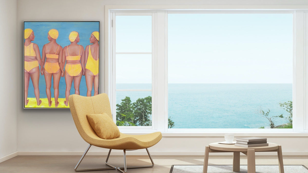 A modern living room scene with a large framed colorful painting of four women in yellow swimwear on the wall, next to a large window overlooking the ocean. 