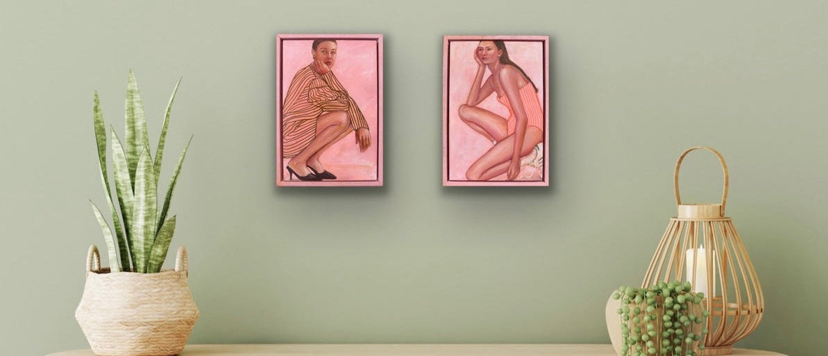 Two small pink framed artworks on a wall above a console table with plants and a lantern.